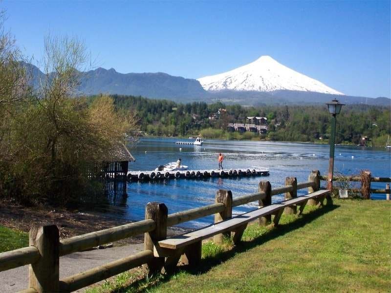 Volcán Villarrica nevado reflejado en el lago con muelle y bosque nativo en el Sur de Chile